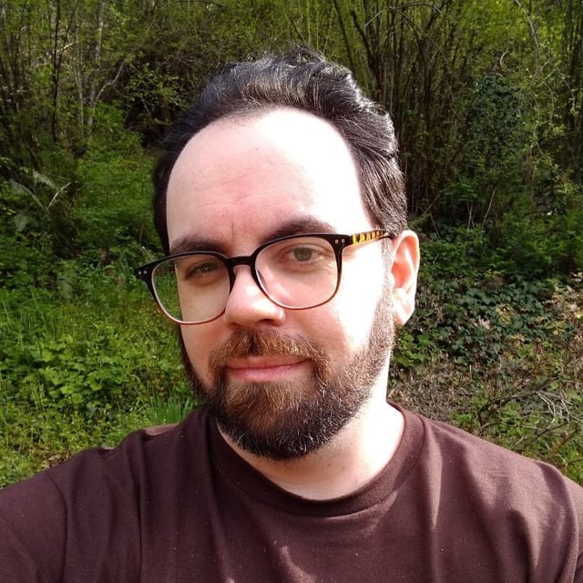 A photo of Yamen, a man wearing glasses with dark hair, a full beard, and curious eyes.